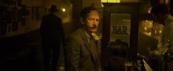 Movie still from “Marlowe” (2022), directed by Neil Jordan – A man wearing a suit and tie standing in a room; Medium shot, Low angle