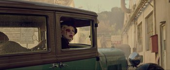 Movie still from “Marlowe” (2022), directed by Neil Jordan – A woman with a face paint looking out of the window of a car; Medium shot, Over the shoulder angle