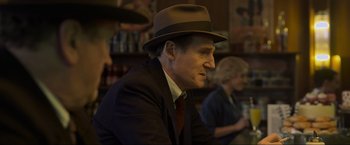Movie still from “Marlowe” (2022), directed by Neil Jordan – An older man wearing a hat sitting at a table; Medium shot, Over the shoulder angle