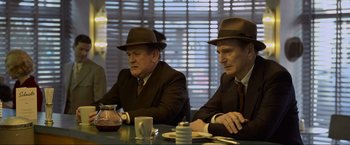 Movie still from “Marlowe” (2022), directed by Neil Jordan – A couple of men sitting next to each other at a table; Medium shot, Over the shoulder angle