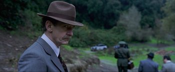 Movie still from “Marlowe” (2022), directed by Neil Jordan – A man in a suit and a hat standing in front of a car; Close Up shot, Over the shoulder angle