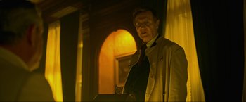 Movie still from “Marlowe” (2022), directed by Neil Jordan – A man standing in front of a window in a room; Medium shot, Low angle