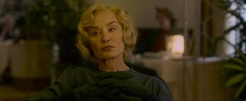 Movie still from “Marlowe” (2022), directed by Neil Jordan – An older woman with blonde curly hair wearing a green sweater; Close Up shot, Over the shoulder angle