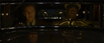 Movie still from “Marlowe” (2022), directed by Neil Jordan – Two men in a car looking out the window at night; Medium shot, Low angle