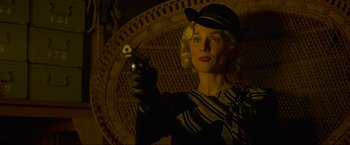 Movie still from “Marlowe” (2022), directed by Neil Jordan – A woman holding a gun while standing in front of a wicker chair; Close Up shot, Low angle