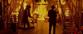 Movie still from “Marlowe” (2022), directed by Neil Jordan – Two men in suits and hats standing in front of a fire; Wide shot, Over the shoulder angle