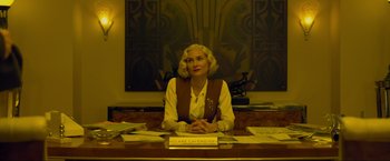 Movie still from “Marlowe” (2022), directed by Neil Jordan – A woman sitting at a desk in front of papers; Medium shot, Low angle