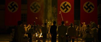 Movie still from “Marlowe” (2022), directed by Neil Jordan – A group of people standing around a stage with flags; Extreme Wide shot, High angle