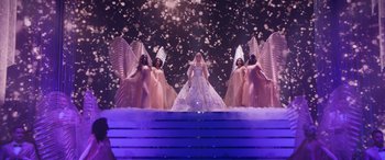 Movie still from “Marry Me” (2022), directed by Kat Coiro – A woman in a white dress standing in front of three angels; Extreme Wide shot, High angle