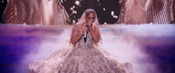 Movie still from “Marry Me” (2022), directed by Kat Coiro – A woman in a long dress singing into a microphone; Wide shot, Over the shoulder angle