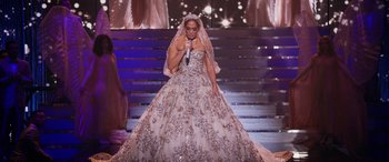 Movie still from “Marry Me” (2022), directed by Kat Coiro – A woman in a dress on a stage with a microphone in her hand; Wide shot, High angle