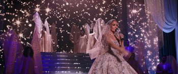 Movie still from “Marry Me” (2022), directed by Kat Coiro – A woman in a white dress is holding a microphone; Wide shot, Over the shoulder angle