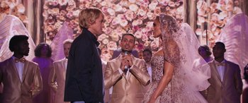Movie still from “Marry Me” (2022), directed by Kat Coiro – A man and a woman standing next to each other while holding a microphone; Wide shot, Over the shoulder angle