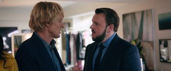 Movie still from “Marry Me” (2022), directed by Kat Coiro – Two men in business suits talking to each other; Medium shot, Over the shoulder angle