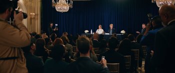 Movie still from “Marry Me” (2022), directed by Kat Coiro – A group of people sitting in a room with microphones; Wide shot, Over the shoulder angle