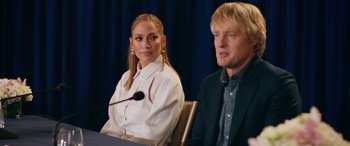 Movie still from “Marry Me” (2022), directed by Kat Coiro – A woman sitting next to a man in front of microphones; Medium shot, Over the shoulder angle