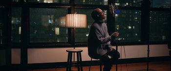 Movie still from “Marry Me” (2022), directed by Kat Coiro – A man sitting on a chair in front of a microphone; Medium shot, Low angle