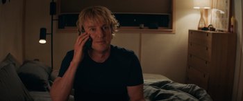 Movie still from “Marry Me” (2022), directed by Kat Coiro – A man sitting on a bed talking on a cell phone; Close Up shot, Low angle