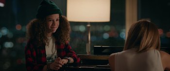 Movie still from “Marry Me” (2022), directed by Kat Coiro – A young woman sitting at a table in front of a lamp; Close Up shot, Over the shoulder angle