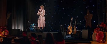 Movie still from “Marry Me” (2022), directed by Kat Coiro – A woman standing on a stage singing into a microphone; Wide shot, Over the shoulder angle