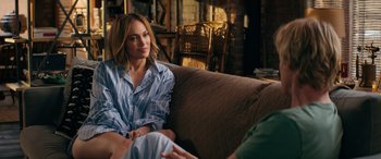 Movie still from “Marry Me” (2022), directed by Kat Coiro – A woman sitting on top of a brown couch next to a man; Medium shot, Over the shoulder angle