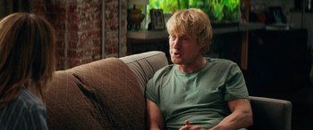 Movie still from “Marry Me” (2022), directed by Kat Coiro – A man sitting on top of a couch in a living room; Medium shot, Over the shoulder angle