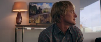 Movie still from “Marry Me” (2022), directed by Kat Coiro – A man in front of a television with a red and blue checkered shirt; Close Up shot, Over the shoulder angle