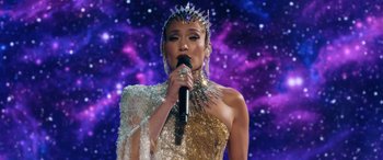 Movie still from “Marry Me” (2022), directed by Kat Coiro – A woman in a gold and silver dress holding a microphone in her hand; Medium shot, Low angle