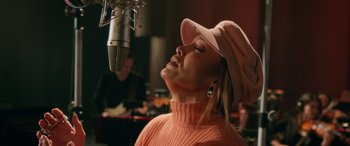 Movie still from “Marry Me” (2022), directed by Kat Coiro – A woman wearing a hat is singing into a microphone; Medium shot, Low angle