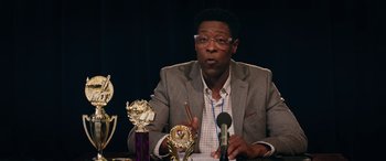 Movie still from “Marry Me” (2022), directed by Kat Coiro – A man sitting at a table in front of a microphone; Close Up shot, Over the shoulder angle