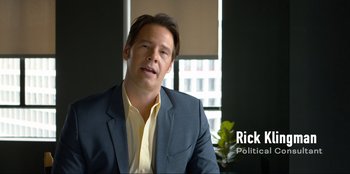 Movie still from “Maximum Truth” (2023), directed by David Stassen – A person wearing a suit and tie; Medium shot, High angle