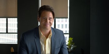 Movie still from “Maximum Truth” (2023), directed by David Stassen – A man wearing a suit and smiling for the camera; Medium shot, Low angle