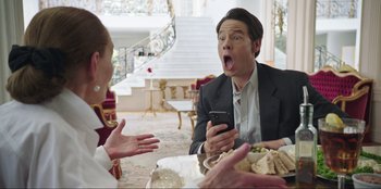 Movie still from “Maximum Truth” (2023), directed by David Stassen – A man in a business suit is holding a cell phone; Medium shot, Over the shoulder angle