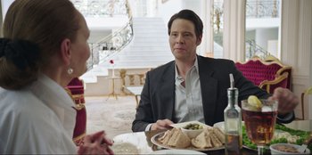 Movie still from “Maximum Truth” (2023), directed by David Stassen – A man sitting at a table with a plate of food in front of him; Medium shot, Over the shoulder angle