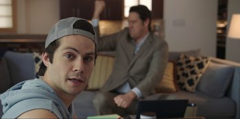 Movie still from “Maximum Truth” (2023), directed by David Stassen – A man sitting on a couch next to another man in a suit; Medium shot, Over the shoulder angle