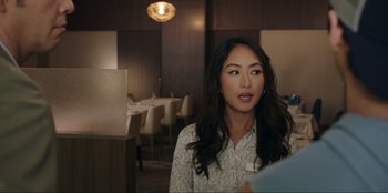 Movie still from “Maximum Truth” (2023), directed by David Stassen – A woman sitting at a table in front of a bunch of tables; Close Up shot, Over the shoulder angle