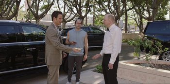 Movie still from “Maximum Truth” (2023), directed by David Stassen – A group of men standing next to each other on a sidewalk; Medium shot, Over the shoulder angle