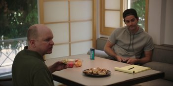 Movie still from “Maximum Truth” (2023), directed by David Stassen – Two men sitting at a table with food on it; Medium shot, Over the shoulder angle