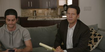 Movie still from “Maximum Truth” (2023), directed by David Stassen – A man sitting on a couch in a living room; Medium shot, Over the shoulder angle