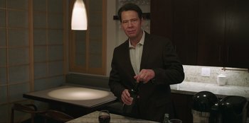 Movie still from “Maximum Truth” (2023), directed by David Stassen – A man in a suit and tie holding a bottle of wine; Medium shot, Over the shoulder angle