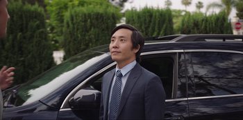 Movie still from “Maximum Truth” (2023), directed by David Stassen – A man standing next to a car in a parking lot; Medium shot, Over the shoulder angle