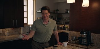 Movie still from “Maximum Truth” (2023), directed by David Stassen – A man standing in front of a counter with a cup; Medium shot, Over the shoulder angle
