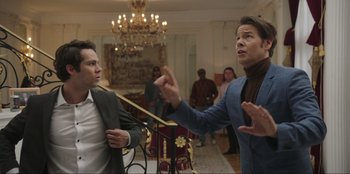 Movie still from “Maximum Truth” (2023), directed by David Stassen – Two men in a room with people in the background; Medium shot, Over the shoulder angle