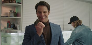 Movie still from “Maximum Truth” (2023), directed by David Stassen – A man in a blue suit talking on a cell phone; Medium shot, Over the shoulder angle