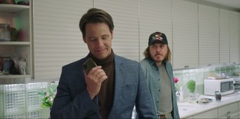 Movie still from “Maximum Truth” (2023), directed by David Stassen – A man in a blue suit and a man in a black hat; Medium shot, Over the shoulder angle