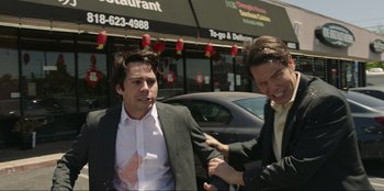 Movie still from “Maximum Truth” (2023), directed by David Stassen – Two men in business suits are outside a restaurant; Medium shot, Low angle