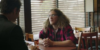 Movie still from “Maximum Truth” (2023), directed by David Stassen – A man sitting at a table with a glass of beer in front of him; Medium shot, Over the shoulder angle