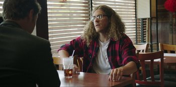 Movie still from “Maximum Truth” (2023), directed by David Stassen – A man sitting at a table with a glass of water; Medium shot, Over the shoulder angle
