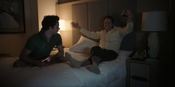 Movie still from “Maximum Truth” (2023), directed by David Stassen – Two men sitting on a bed and one is holding a glass of wine; Medium shot, High angle