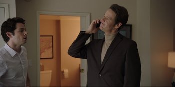 Movie still from “Maximum Truth” (2023), directed by David Stassen – A man talking on a cell phone while wearing a suit; Medium shot, Over the shoulder angle
